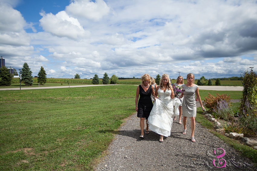 05-bride-with-mom-and-bridesmaids-walking-on-path-with-blue-cloudy-sky-michigan-wedding-photographer